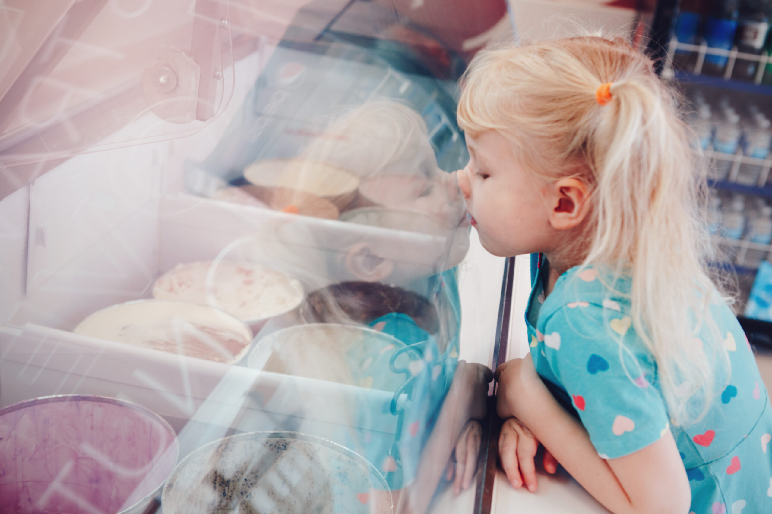 Blonde girl looking at ice cream through window